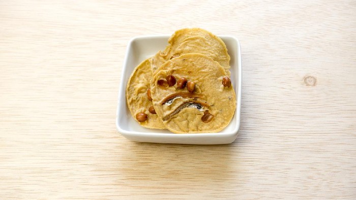 Rempeyek kacang bilis or Crunchy Peanut Crisp with dried anchovies on wooden surface. Concept of Malaysian traditional Malay Raya festive meal. Slightly de-focused and close up shot. Copy space.