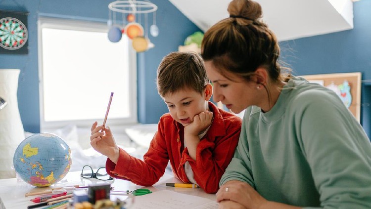 Photo of a young boy being homeschooled by his mother in his bedroom