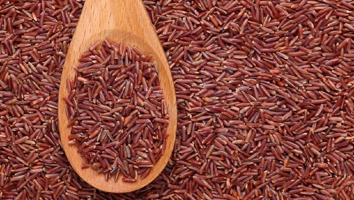 Red rice in a wooden spoon on red rice background.Please see: