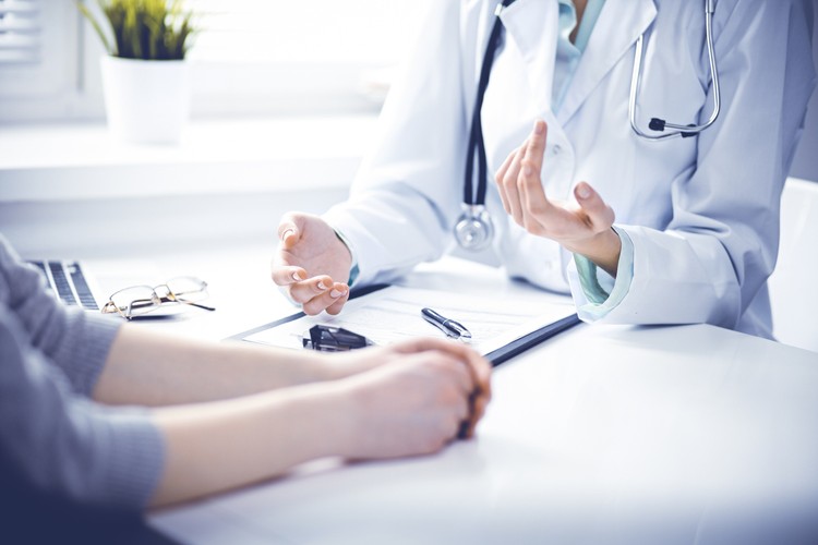 Close up of doctor and  patient  sitting at the desk near the window in hospital