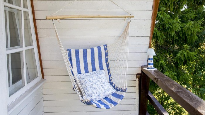 Blue and white striped pattern string and cotton hammock hanging chair, white painted wooden board background. Relaxing in countryside home garden balcony outdoors on summer day concept.