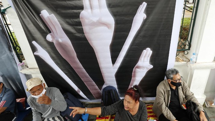 Pro-democracy protesters sit in front of a poster of the three finger symbol of resistance during a protest outside Thammasat University in Bangkok, Thailand, Saturday, Sept. 19, 2020. Protesters gathered Saturday in Bangkok for what was expected to be the biggest rally yet in an ongoing campaign calling for a new election and democratic reforms. (AP Photo/Sakchai Lalit)