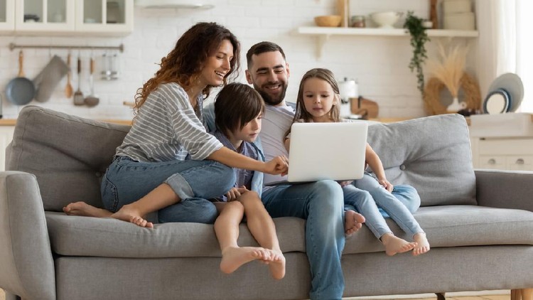 Happy young family with little kids sit on sofa in kitchen have fun using modern laptop together, smiling parents rest on couch enjoy weekend with small children laugh watch video on computer at home