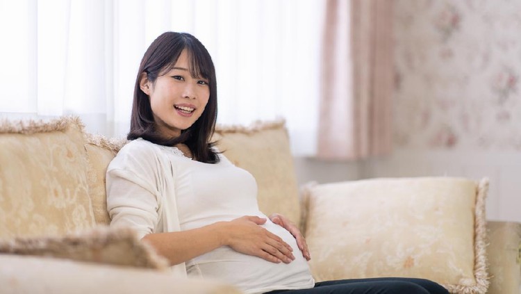 Pregnant woman sitting on couch and holding her abdomen