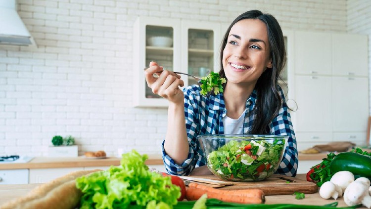 Diet makan salad Healthy lifestyle. Good life. Organic food. Vegetables. Close up portrait of happy cute beautiful young woman while she try tasty vegan salad in the kitchen at home.