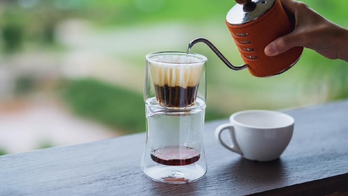 Closeup image of a hand pouring hot water from kettle to make drip coffee with blurred nature background