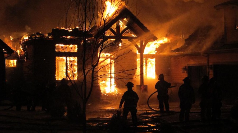 Firemen use a fire hose to try and put out a house fire during a snowfall.