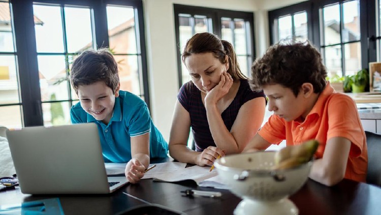 Mother homeschooling teenage boys from home on a dinner table.They are self-isolating from Covid-19 and preparing for back to school.
