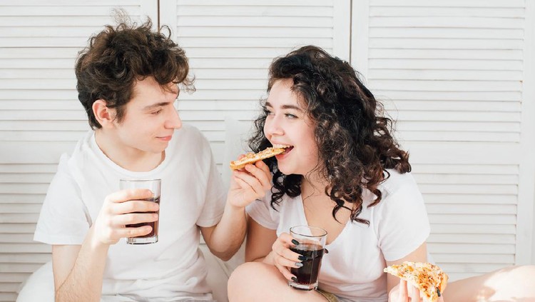 Loving couple watching TV in bed and eating pizza. The concept of love and romance. Toning.