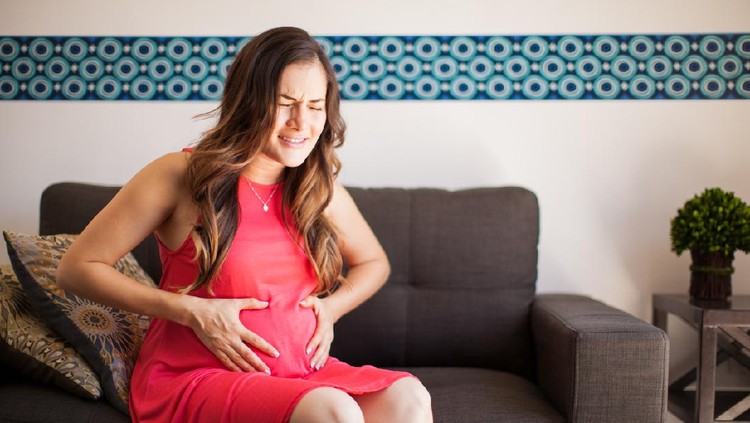 Young pregnant brunette sitting in the living room and having some contractions
