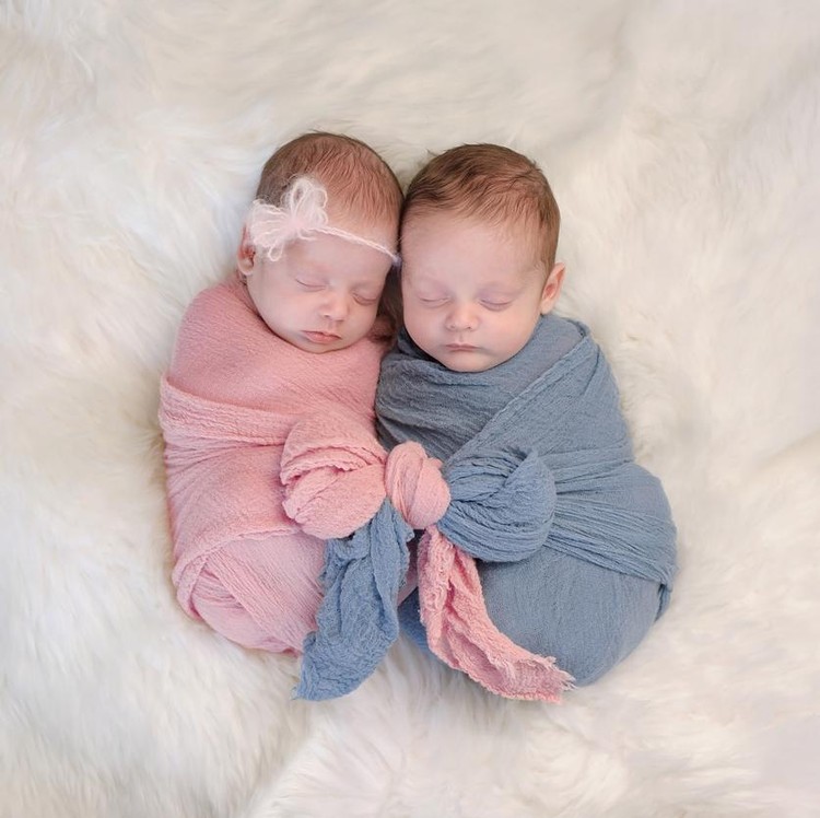 Two month old, boy and girl fraternal twin babies. They are sleeping and swaddled together in pink and blue wraps that are tied together in a bow.