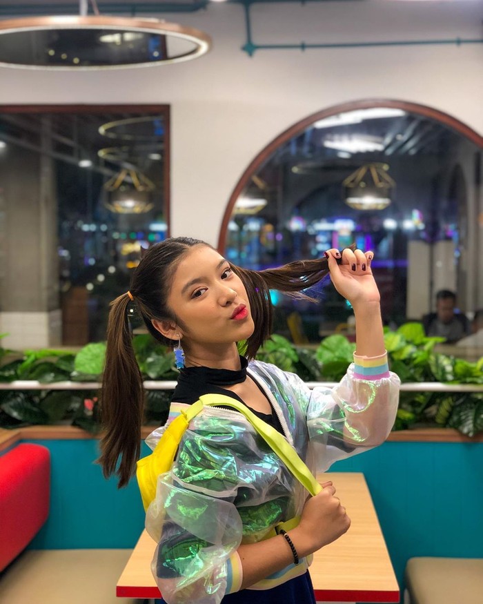 Outfit bernuansa neon juga jadi pilihan terbaik untuk menonjolkan kesan tren 90-an. Perpaduan jaket bomber transparan dan v-neck polos berwarna hitam membuat penampilan terlihat nyentrik tapi menawan. Beri sentuhan girly pada gaya rambut dan nuansa colorful dengan memilih tas berwarna kuning cerah. (Foto: www.instagram.com/tiaraandini/)