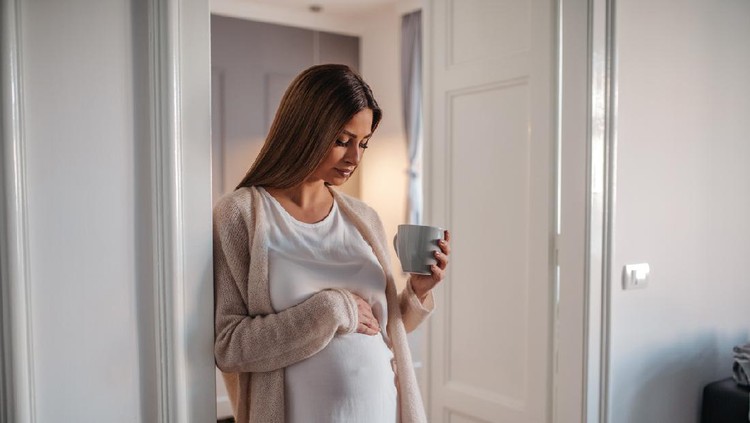 Beautiful pregnant woman drinking coffee indoors.