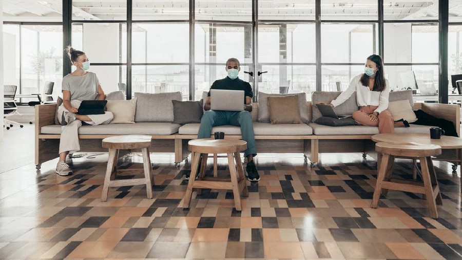 Businesspeople working and maintaining social distance on a sofa in a modern office