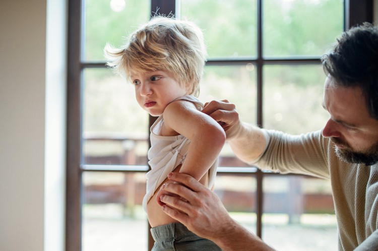ruam Father with small sick unhappy son indoors at home, checking his hurt back.