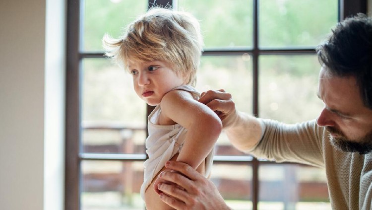 ruam Father with small sick unhappy son indoors at home, checking his hurt back.
