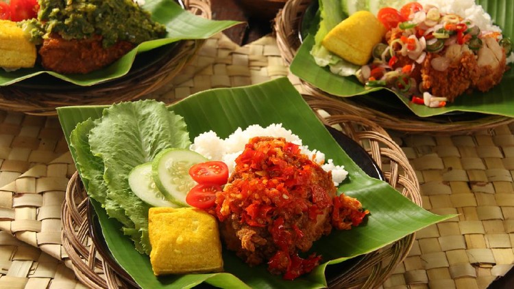 Ayam Geprek, the popular fusion street food dish of southern fried chicken served with traditional spicy condiments from regional cuisines in Indonesia. Here each of the chicken piece is topped with a popular condiment, such as Sambal Lado (lightly red chili paste) and Sambal Lado Mudo (green chili paste), both from West Sumatra, and Sambal Matah (chili pepper, lemon grass and shallot salsa) from Bali. The chicken and condiment are served with steamed rice, yellow tofu, and fresh vegetables. The dish is plated on a ceramic plate lined with banana leaf; which then placed on a woven stick plate.