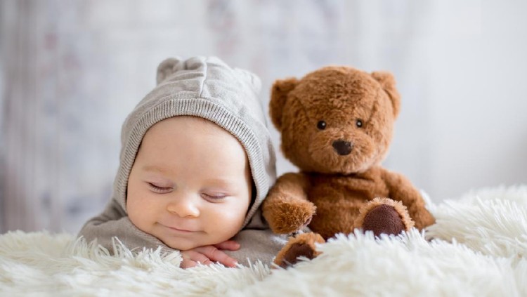 bayi Sweet baby boy in bear overall, sleeping in bed with teddy bear stuffed toys, winter landscape behind him