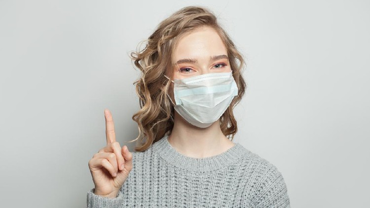 Pretty woman wearing a medical mask and pointing finger up on white background