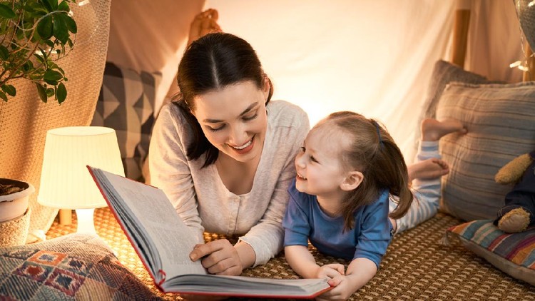mendongeng Family bedtime. Mom and child daughter are reading a book in tent. Pretty young mother and lovely girl having fun in children room.