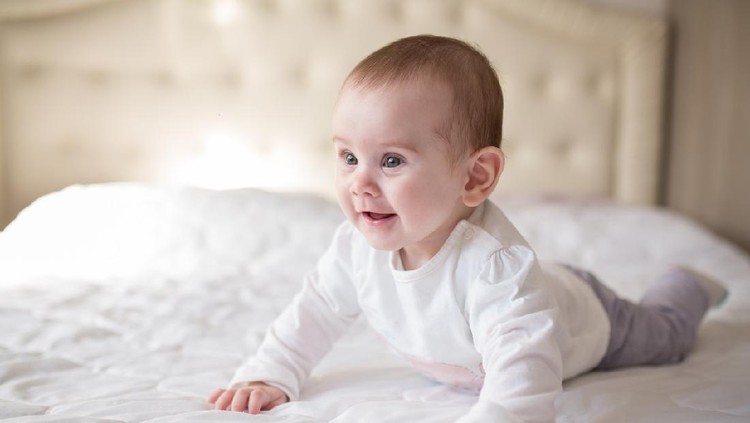 Cute little 10 months old baby lying on the bed and looking into the camera.