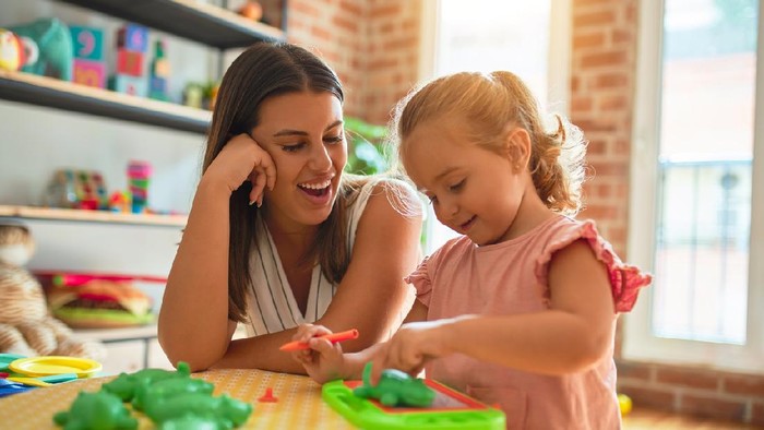 Beautiful teacher and blond student toddler girl drawing using digital board at kindergarten