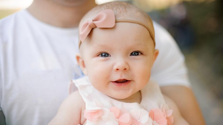 Portrait of little cute smiling baby girl dressed in pink dress and bow in father hands