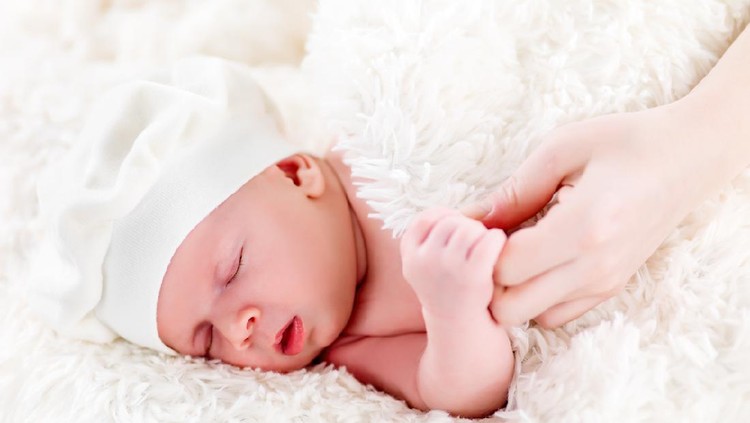 Above view of a baby boy wearing a cute hat and holding mother's hand.