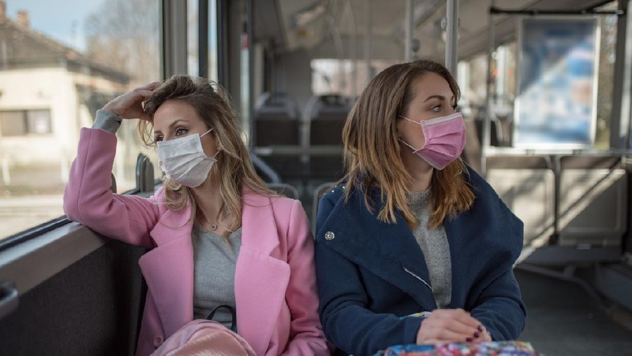 Two young women at public transport during virus epidemic. Two women sitting at public transport wearing pollution masks.