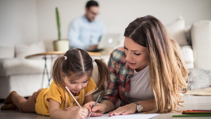 Getting help with my tasks. Little girl working her homework with mother. Focus is on foreground.