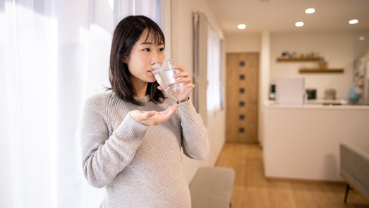 Pregnant woman taking medicine in living room