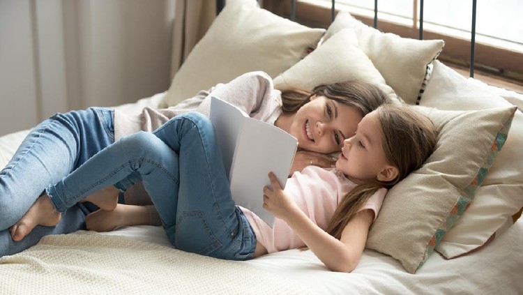 Daughter and mom resting lying on bed resting having lazy weekend at home, little kid girl holding fairy tale book reading interesting story to mum spend time together, good hobby, smart child concept