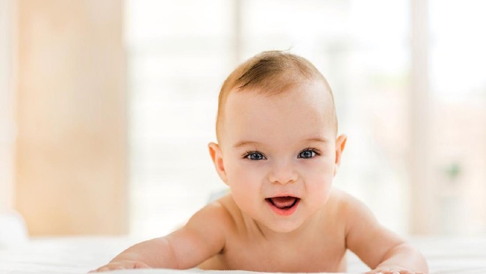 Portrait of happy baby boy lying down in bed and looking at camera.