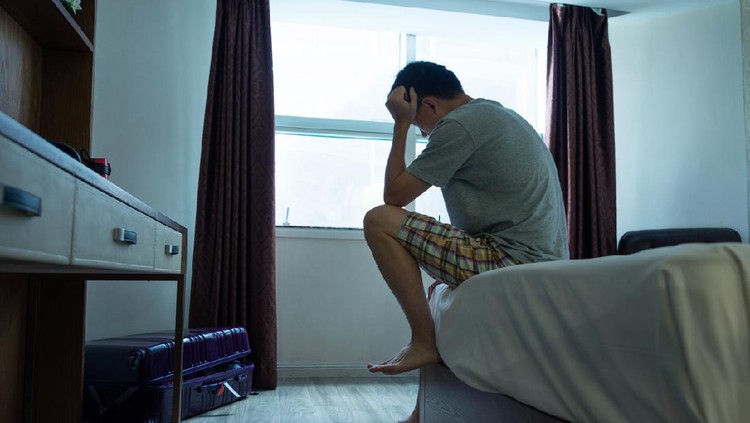 Man sitting on bed with head in hands