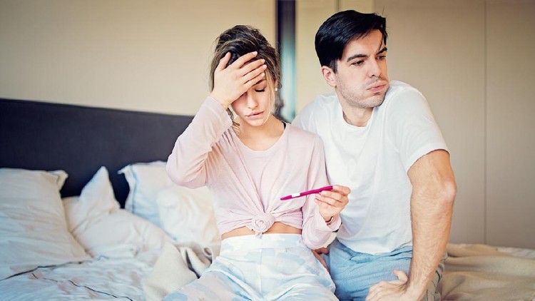 Shocked couple is looking positive pregnancy test in the bedroom