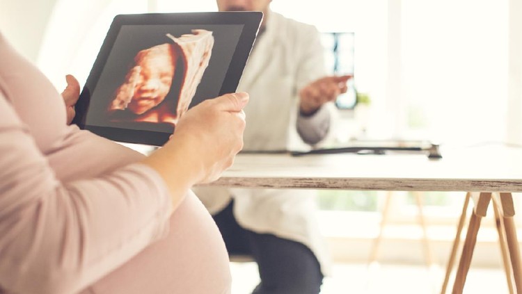 Pregnant woman looking at ultrasound image of her baby at doctor's office.