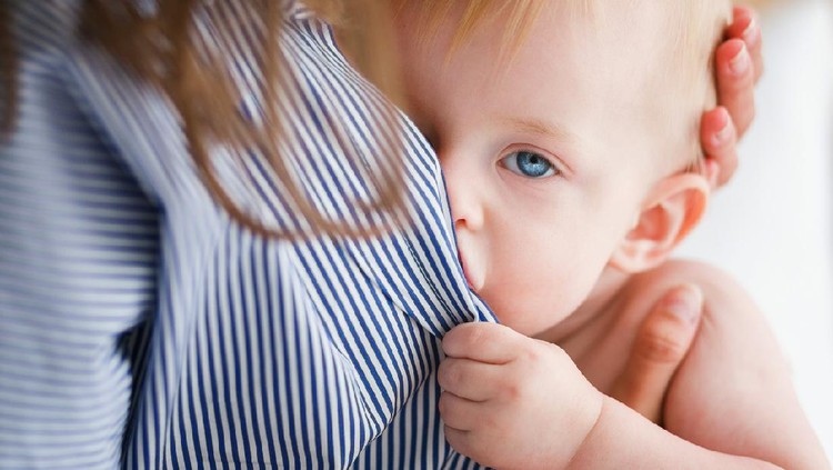 Baby is fed mother's milk looking at camera. Close up head shot.