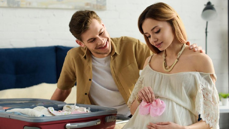 pregnant wife and smiling husband preparing suitcase for hospital