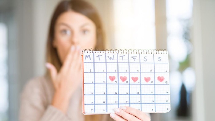 Young beautiful woman holding menstruation calendar at home cover mouth with hand shocked with shame for mistake, expression of fear, scared in silence, secret concept
