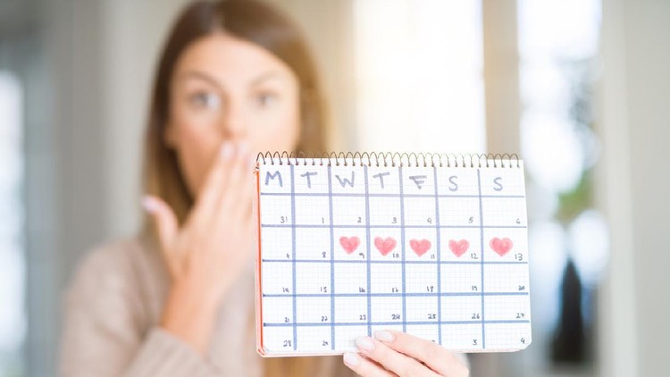 menstruasi Young beautiful woman holding menstruation calendar at home cover mouth with hand shocked with shame for mistake, expression of fear, scared in silence, secret concept