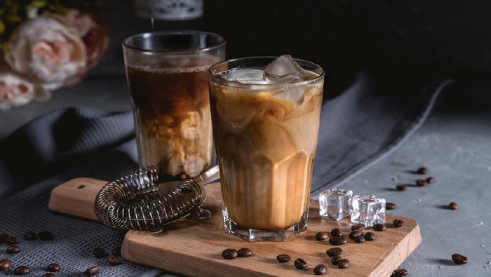 Iced coffee in a tall glass with cream on dark background