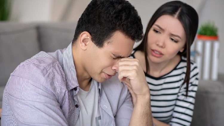Difficult situation. Young man with eyes closed hand near the eyes, and a sympathetic woman carefully looking and talking.