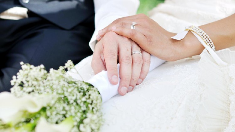 Husband and wife hands on wedding, holding flowers.
