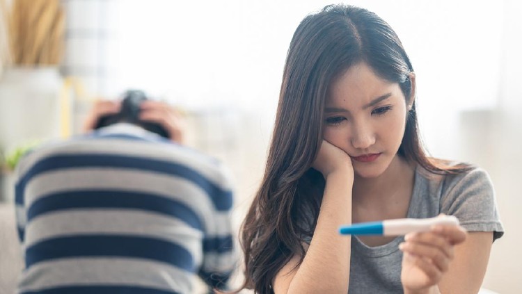 tes kehamilan Disappointed Asian woman sitting bed when see the pregnancy test result. Girl feels worry and not ready to be a mother. Man feeling stress about the future kid holding head. Unprepared sexual problem.