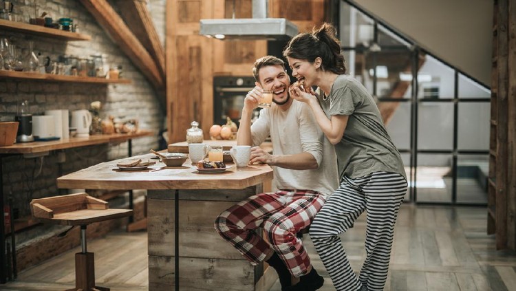 Young happy couple spending their morning together in the kitchen while woman is eating and man is drinking juice.