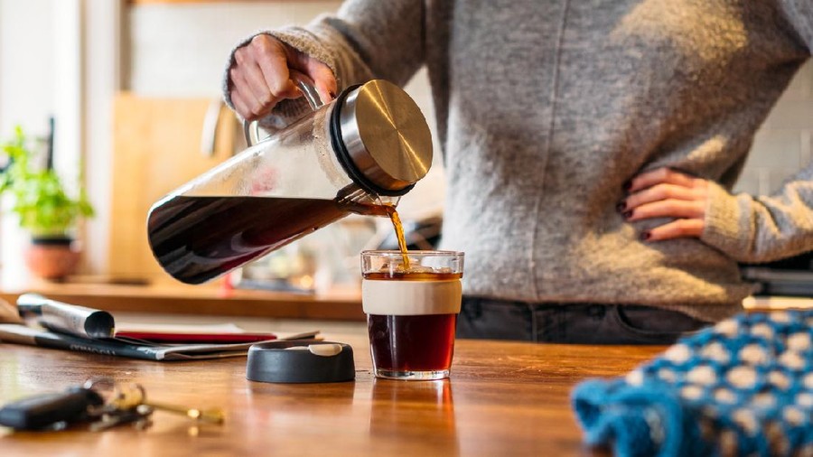 A woman pouring cold-brew coffee into a re-usable mug in the kitchen.