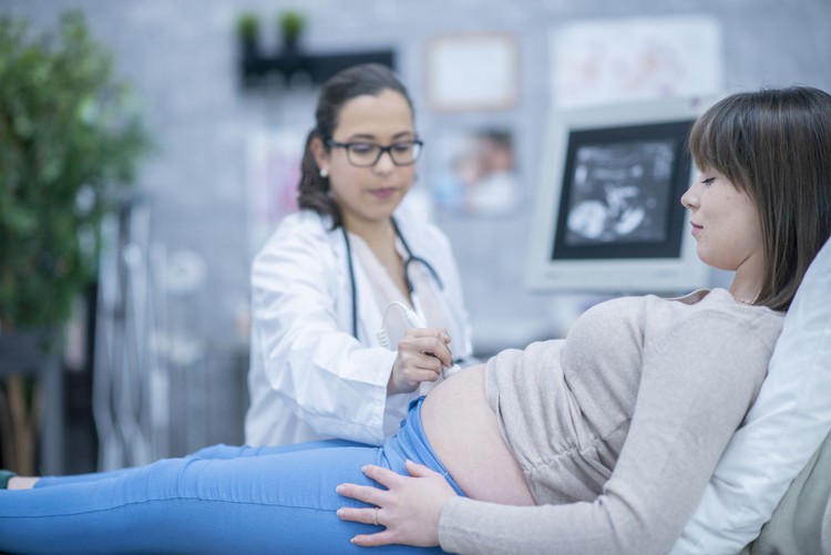 A pregnant woman and her female doctor are indoors in a hospital. The doctor is performing an ultrasound.