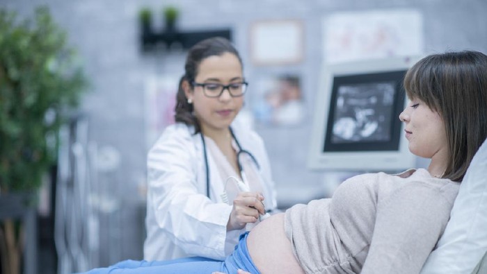 A pregnant woman and her female doctor are indoors in a hospital. The doctor is performing an ultrasound.