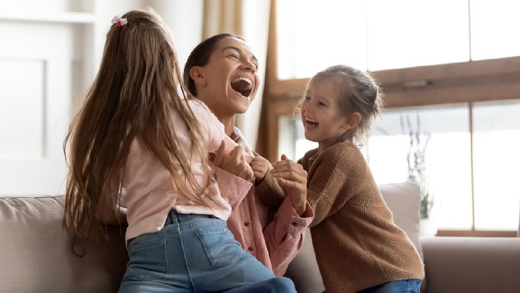 Cheerful positive family cute small funny kids children daughters enjoying tickling playing lifestyle game with young happy mum embracing laughing having fun relaxing sitting on sofa at home together