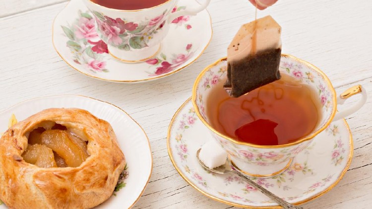 menyeduh teh A high angle close up shot of a hand steeping a tea in two dainty teacups and a miniature galette.